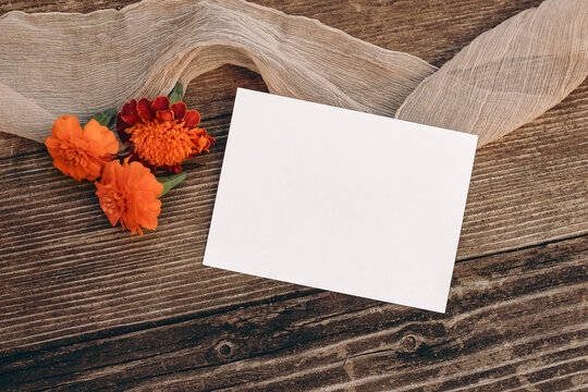 Autumn wedding still life scene. Blank greeting card mock-up. Floral composition. Orange tagetes flowers on old wooden table background. Flat lay, top view. Halloween, Dia de los Muertos holiday.