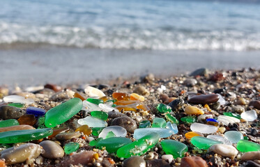Many wet colored glass polished by the sea on the beach on a blurred background of the oncoming wave