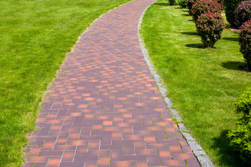 curved stone tile pavement crescent, path in park landscaped with green grass and bushes, garden landscape on a sunny summer day.