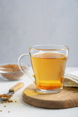 Helba or golden tea made of fenugreek annual plant seeds served in glass cup with grains in spoon on white wooden table at kitchen used in local medicine of Egypt