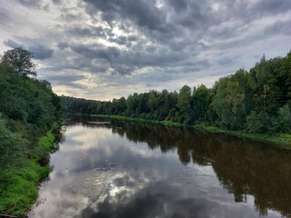 Fototapeta na wymiar Green banks of the Gauja River in the Gauja National Park, Latvia. The clouds are beautifully reflected in the calm water of the river. Silence and solitude with nature.