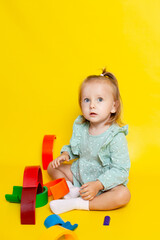Portrait of a cute baby girl with blue eyes on a yellow background, playing with a rainbow designer. educational games and toys. Teaching the child. Color. A place for text.