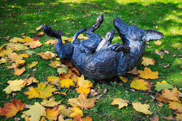 Statue of a frolicking dog lying on its back on the lawn