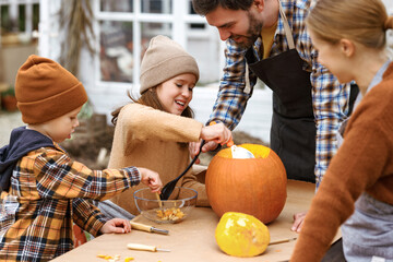 Happy young family carving pumpkins in backyard, children making jack-o-lantern with parents