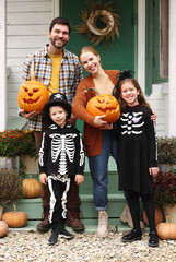 Young happy family parents with kids standing on house porch during Halloween holidays