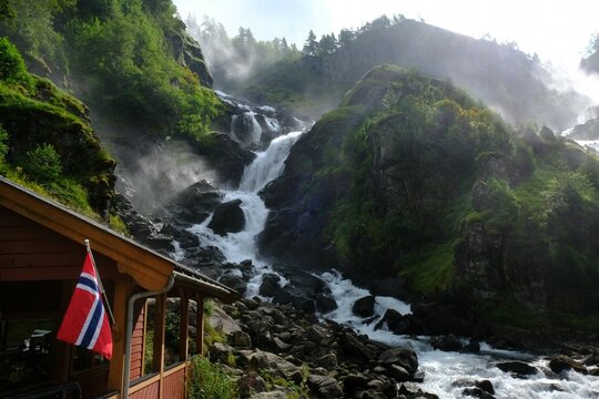 A beautiful landscape with the Latefossen Waterfall and Espelandsfossen Waterfall in Norway. View with Norwegian flag on wooden building.