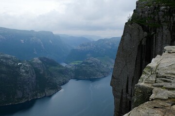 Preikestolen (Prekestolen, Pulpit Rock) is famous tourist attraction near Stavanger, Norway. Preikestolen is steep cliff which rises above Lysefjord. Lonely woman in yellow jacket is standing on cliff