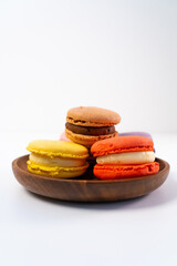 Multicolored macarons on a wooden plate on a white background.