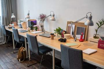 Part of classroom or office with several desks and chairs with supplies standing along wall