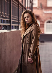 Young smiling woman walking on the street city wall background in brown coat and black shoes near the old bulding with big windows. Autumn