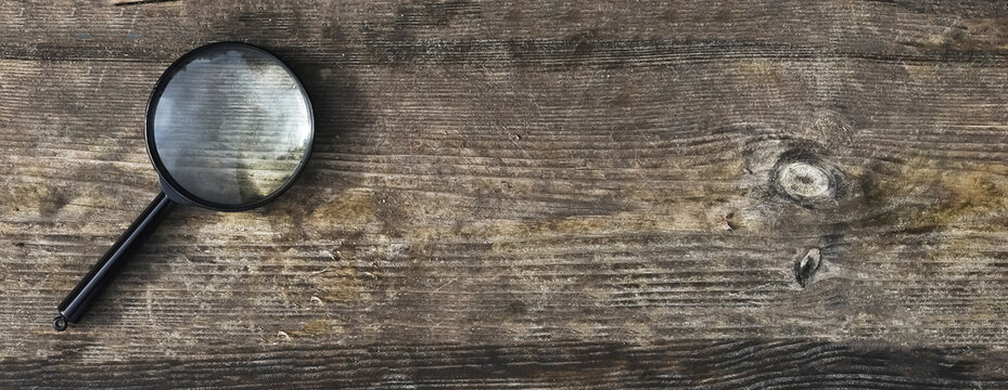 Magnifying lens on wood aged background with copy space for text. Wooden horizontal banner with copyspace.