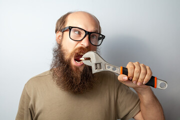Funny male pulling out tooth with wrench, having foolish expression, looks away with crossed eyes,...