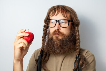 Pensive scientist with braids holding apple in hand, looking away with thoughtful expression, bald bearded man wearing T-shirt and glasses. Indoor studio shot isolated on gray background. - obrazy, fototapety, plakaty