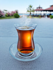 Turkish tea served in tulip-shaped glass on a small saucer blurred nature background. Summer holiday background.