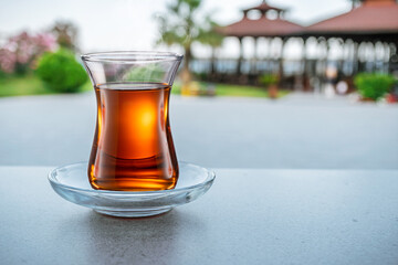 Turkish tea served in tulip-shaped glass on a small saucer blurred nature background. Summer holiday background.