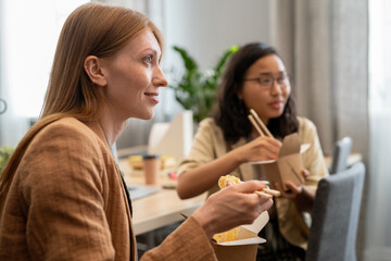 Happy young businesswoman and her colleague eating chinese wok at lunch break in office