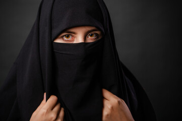 Close up portrait of young, adult woman in black burqa  with hidden face, isolated on black...