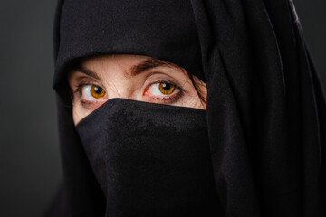 Close up portrait of young, adult woman in black burqa  with hidden face, isolated on black background.