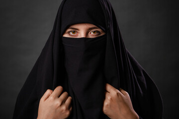 Close up portrait of young, adult woman in black burqa  with hidden face, isolated on black...