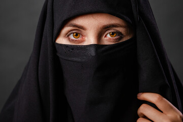 Close up portrait of young, adult woman in black burqa  with hidden face, isolated on black background.