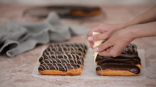 Pastry chef pours white chocolate on French eclairs. 
