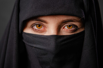Naklejka premium Close up portrait of young, adult woman in black burqa with hidden face, isolated on black background.