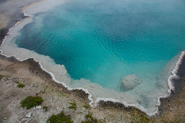 Abstract close up of edge of deep teal hot springs in Yellowstone National Park. Unusual crystal-like edge of sulfur hot springs of teal, blue, and gray. With white sulfur build up around the edge. 