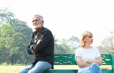 Offended mature man and woman sitting on different sides of bench outdoors at park. Old man and his wife ignoring and not speaking each other after conflict or fight. Relationship problems and upset.