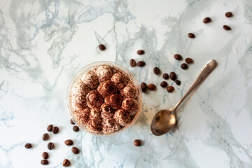 Perfect freshly made Italian tiramisu with cacao. Tiramisu portion on a white marble background. Delicious no bake tiramisu ready-to-eat. Delivery. A plastic cup restaurant dish delivery.Copy space