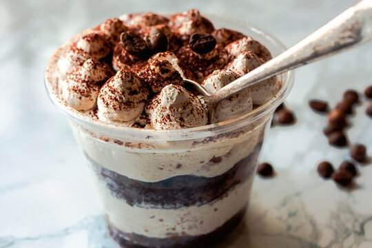 Served Italian dessert Tiramisu, cream, cocoa powder in a plastic take away cup. restaurant dish delivery..Close up.Selective focus