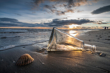 Bouteille en verre échouée sur une plage au coucher de soleil.	