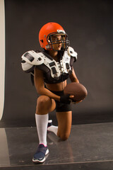 Young woman with braids and american football shoulder pads, helmet and ball