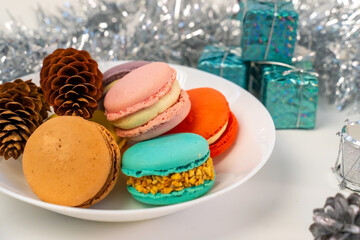Multicolored French cookies in a white plate on a tinsel background.