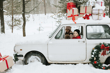Children boy and girl with a dog driving a retro car decorated for Christmas among the winter forest in the village, the concept of a family Christmas and winter holidays
