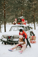 Children boy and girl with a dog stay near a retro car decorated for Christmas among the winter forest in the village and having fun with sledge, concept of family Christmas and winter holidays
