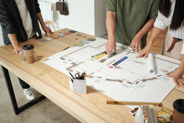 Team of contemporary engineers discussing color palette over blueprint with sketch