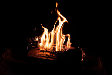 Fire in the fireplace on a dark background. Firewood in flames. An intimate atmosphere by the fire.