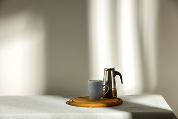 A table with a tablecloth and a lift, fresh coffee in a teapot against the background of a minimalist wall with a shadow and sun falling on a winter morning 