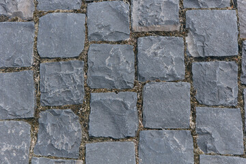 Paved with square granite pavement of dark gray color. The pavement laid with square stone cobbles of granite. 