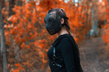 a girl in a bdsm costume and a black mask in a red forest.an idea for halloween.