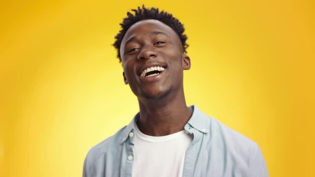 Young african american guy cheering happily, shaking fists and laughing to camera, supporting over yellow background