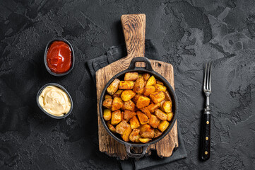 Patatas bravas, spicy potatoes, a Spanish dish with fried potato and a spicy garlic sauce. Black background. Top view