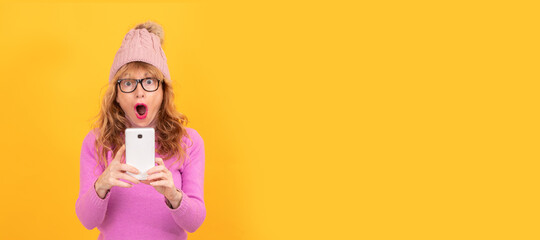 woman isolated on background wearing winter clothes looking surprised at mobile phone, space for text