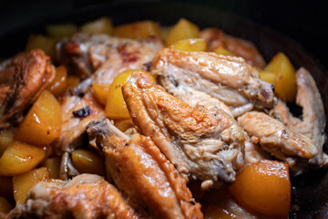 Fried chicken wings with potatoes are cooked in a pan, close-up with shallow depth of field