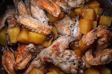 Fried chicken wings with potatoes are cooked in a pan, close-up with shallow depth of field