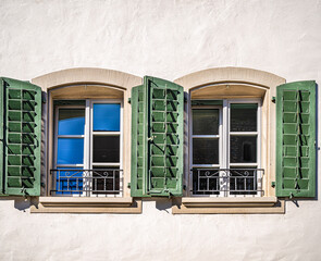 Two windows with green wooden shutters in the wall of an old swiss house