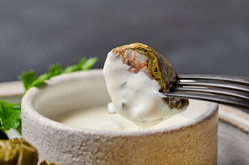 Macro piece of dolma with sour cream on black fork, stuffed grape leaves with rice, meat and parsley. Selective focus