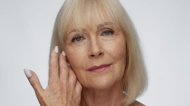 Confident attractive senior woman with wrinkled skin looking at camera, caressing her face with hand with dark spots
