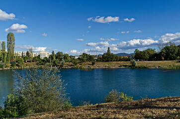 Fototapeta premium Autumn panorama of part of the neighborhood by the lake with green trees, shrubs and sunburned grass, Drujba, Sofia, Bulgaria