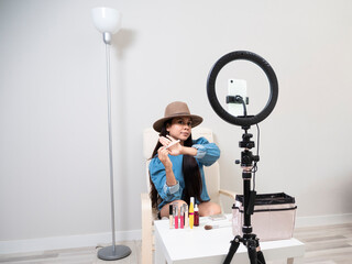 Young Latina content creator girl doing a makeup blog with different feminine products on a chair with a white table and a carpet